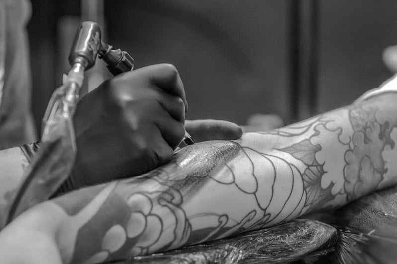 A man is getting a tattoo on his upper arm. The tattoo artist is using a tattoo machine to apply ink to the man's skin. 